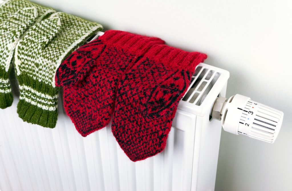 Two pairs of knitted gloves drying on the radiator with thermostat